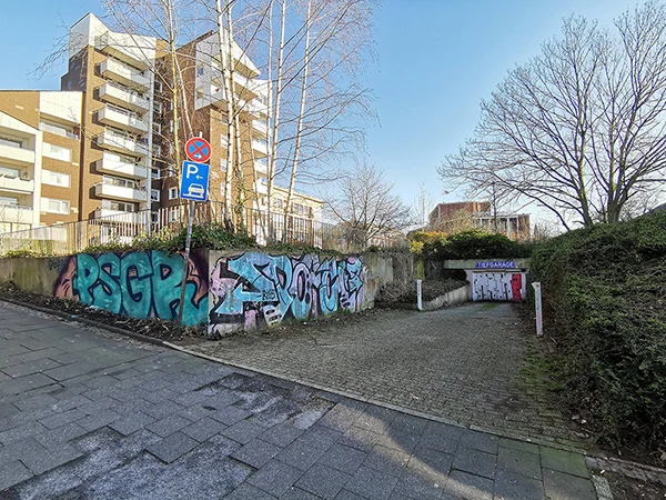 Der ehemalige Bunker Westfalenplatz in Bochum. Die Reste der Außenwände des Tiefbunkers sind links zu sehen. Rechts ist die Einfahrt zu einer Tiefgarage, die hinter dem Bunker angelegt worden ist.